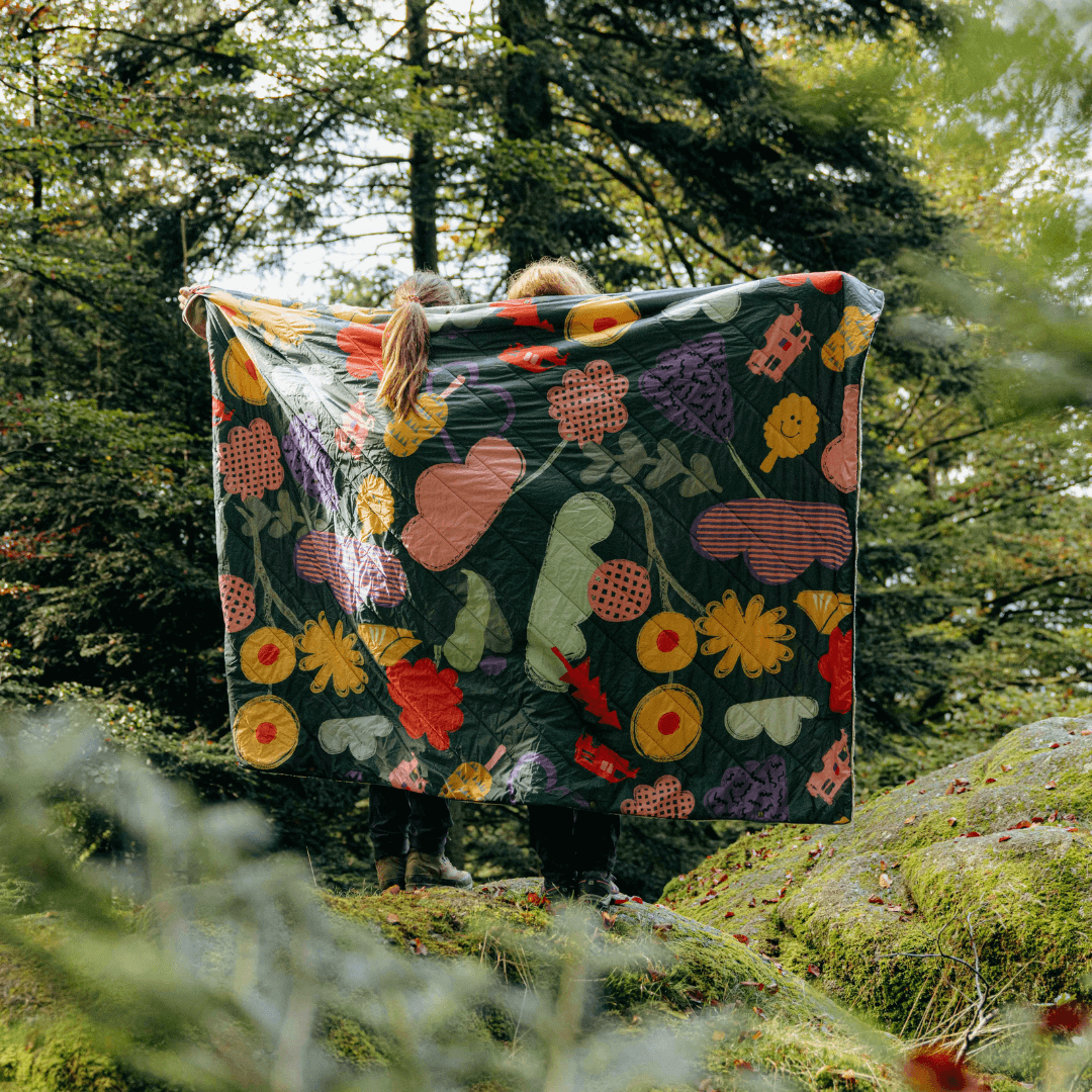 zwei Personen halten eine bunte Decke aus im Wald 